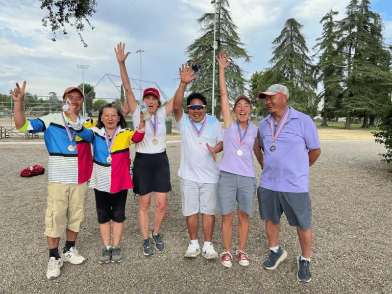 Groupe de personnes célébrant une victoire lors d’un tournoi de pétanque à l’extérieur.