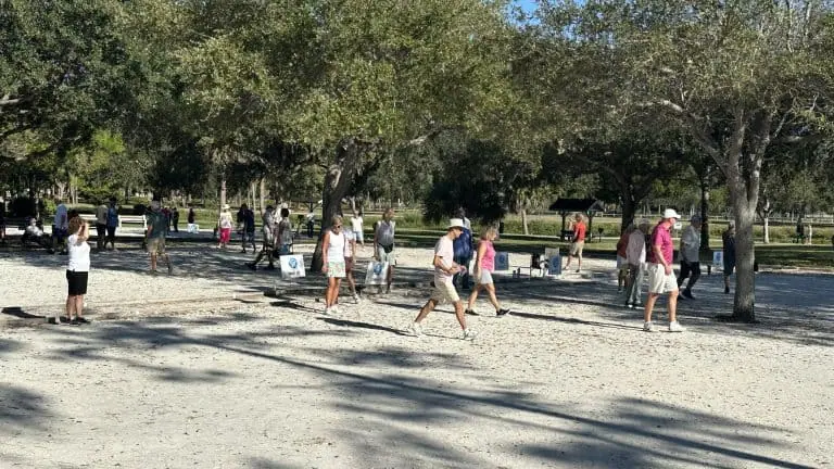 Personnes jouant à la pétanque dans un parc avec des arbres et une surface de gravier.