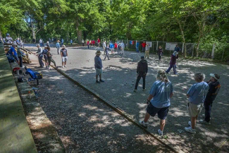 Personnes jouant à la pétanque sur un terrain de gravier dans un parc.