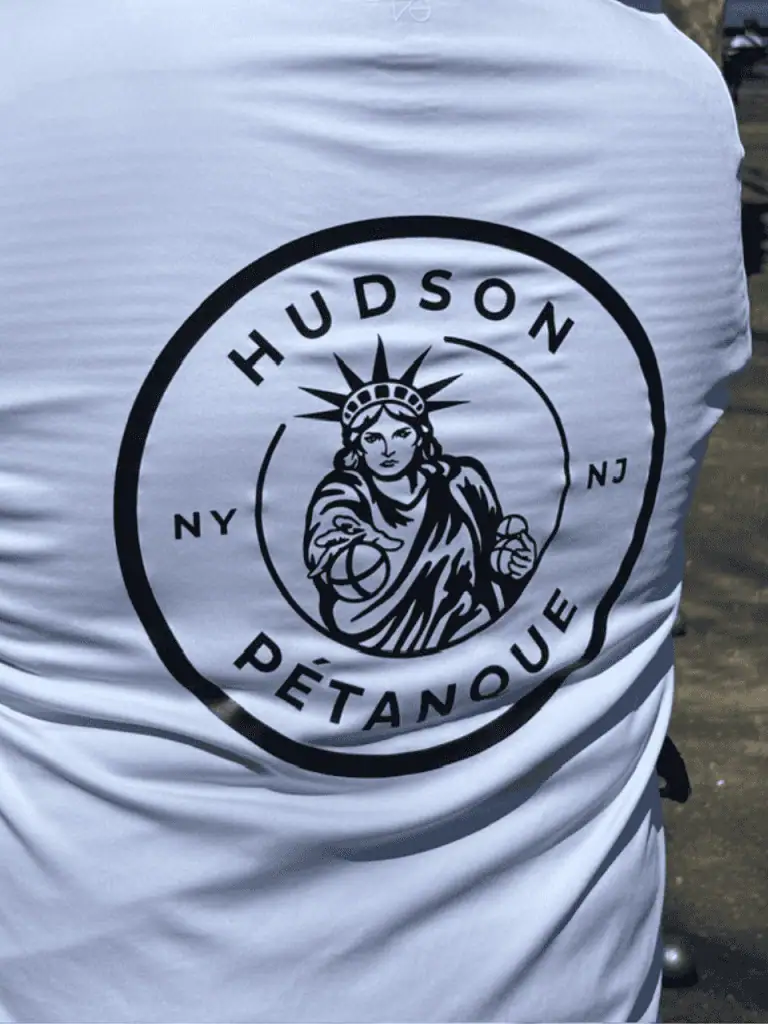 Logotipo de Hudson Petanque en una camiseta blanca, con la Estatua de la Libertad y New Jersey.
