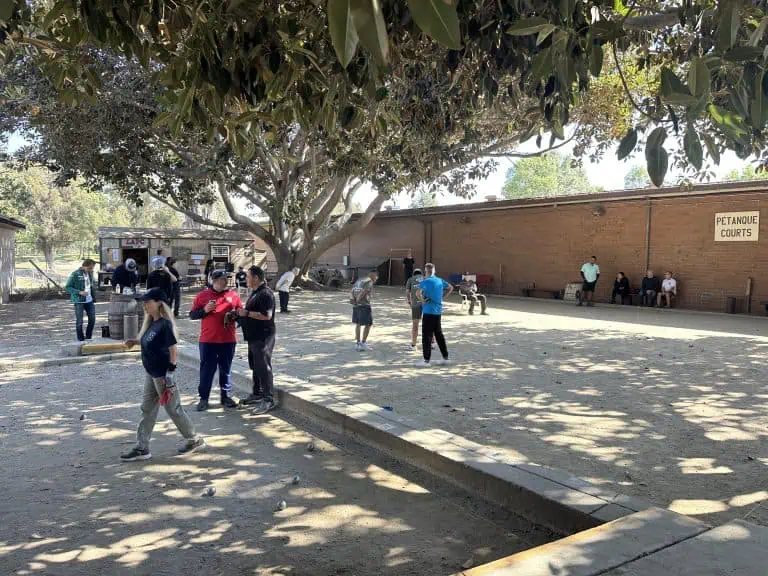 Personnes jouant à la pétanque sur les terrains extérieurs de Petanque Central par temps ensoleillé.