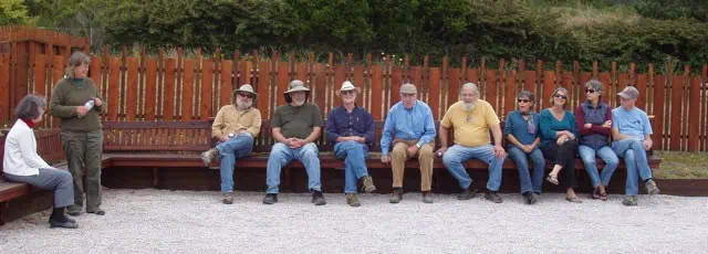 Grupo de personas jugando petanca al aire libre en una cancha de grava con una cerca de madera de fondo.