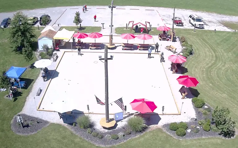 Terrain de pétanque extérieur Petanque Central au Zanesfield Petanque Club avec des parasols colorés et des joueurs.