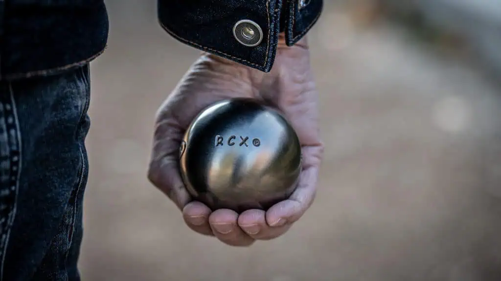 Close-up of a hand holding an Obut RCX petanque ball for review.