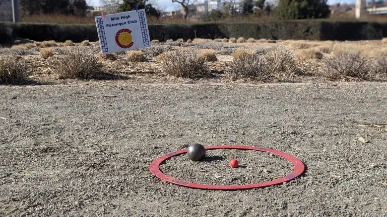 Mise en place d’une partie de pétanque avec une boule argentée, un cercle rouge et un petit cochonnet orange sur un terrain de gravier.