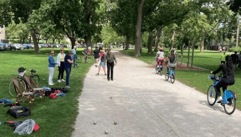 A lush park scene with people playing petanque on a sunny day.